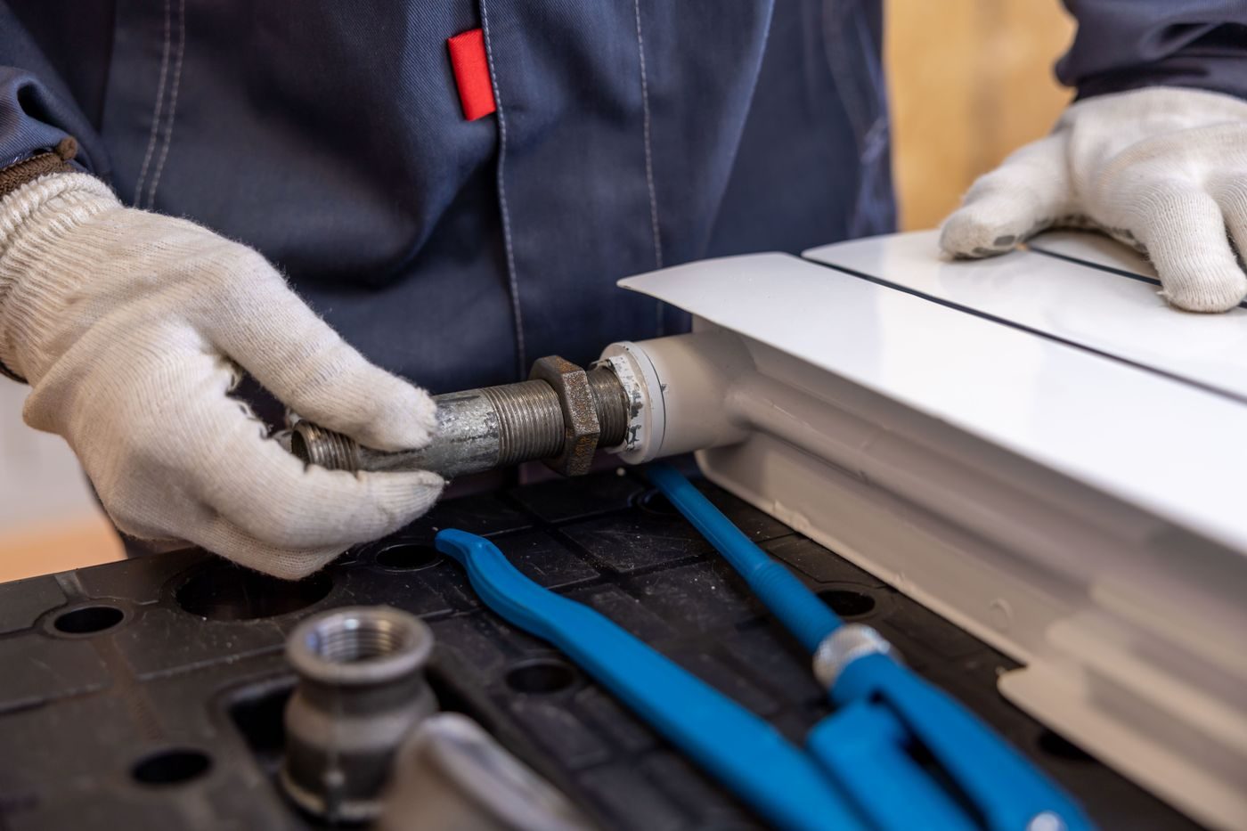 Gloved hands tightening a pipe fitting with blue pipe tools close by