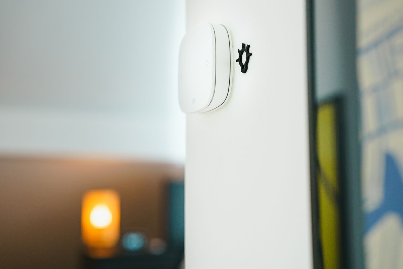 Small white sensor unit mounted on a plain wall with a warm lamp glow behind