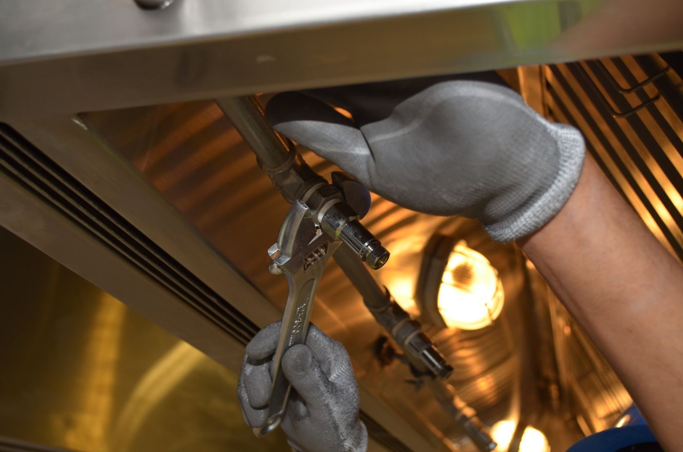 Gloved hands holding an adjustable spanner on a gas pipe joint under warm work light